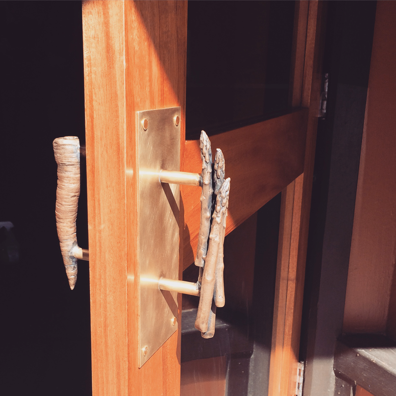 Custom sculptural bronze door handles mounted on a wooden door, featuring organic, branch-like forms and hand-forged texture, designed and crafted by Alexis Pavlantos.