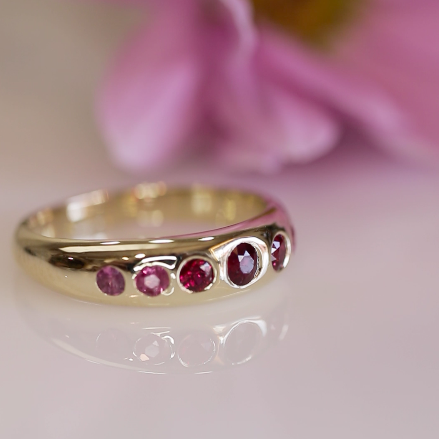 Custom gold band set with five pink sapphires in bezel settings, handcrafted by Albuquerque-based New Mexico jeweler Alexis Pavlantos, shown in a soft studio setting.