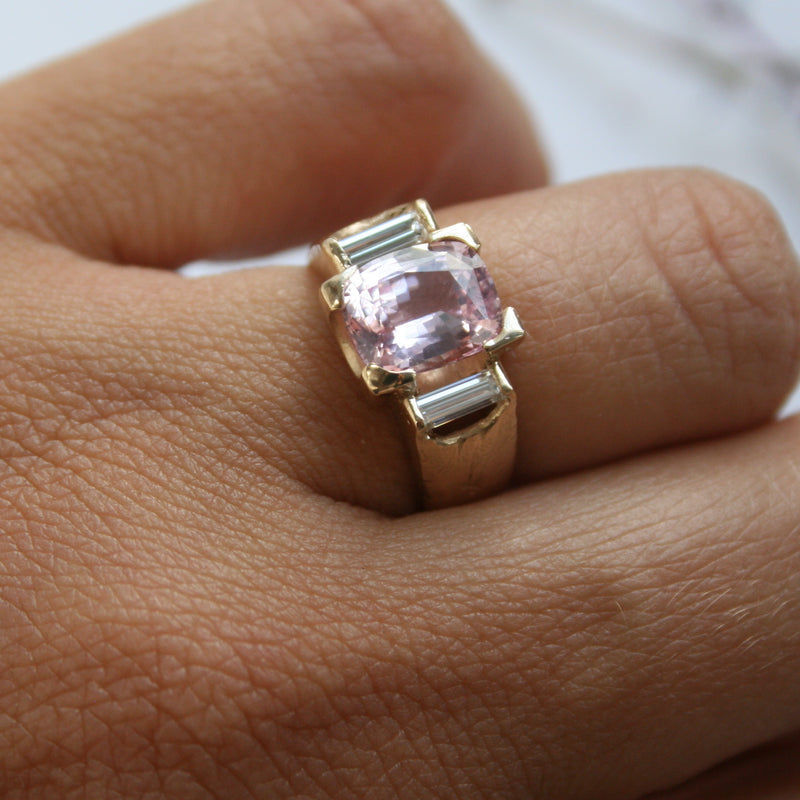 Custom pink sapphire engagement ring with baguette diamond accents in hand-textured gold, shown worn on the hand, handcrafted by Albuquerque-based New Mexico jeweler Alexis Pavlantos.