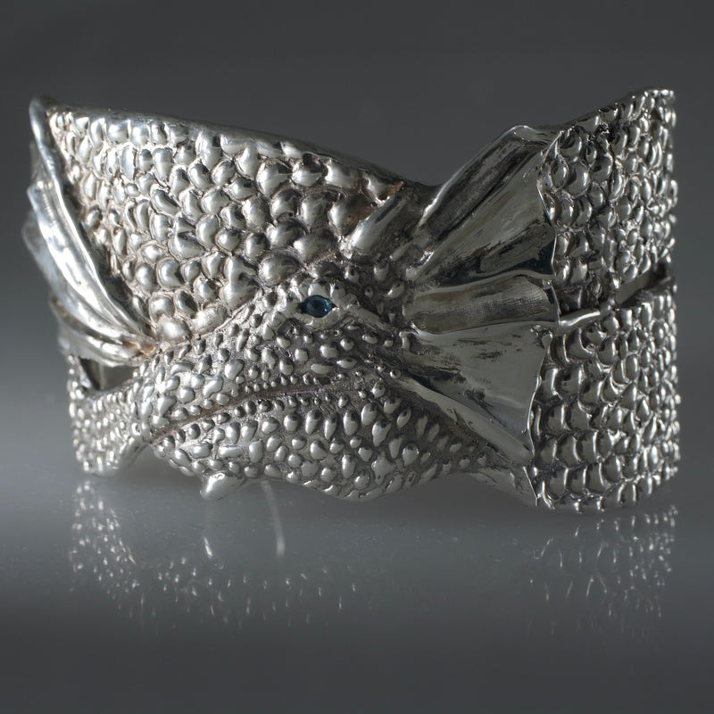 Handcrafted sculptural silver dragon cuff bracelet with textured details and gemstone eyes, created by Albuquerque-based jeweler Alexis Pavlantos in New Mexico.