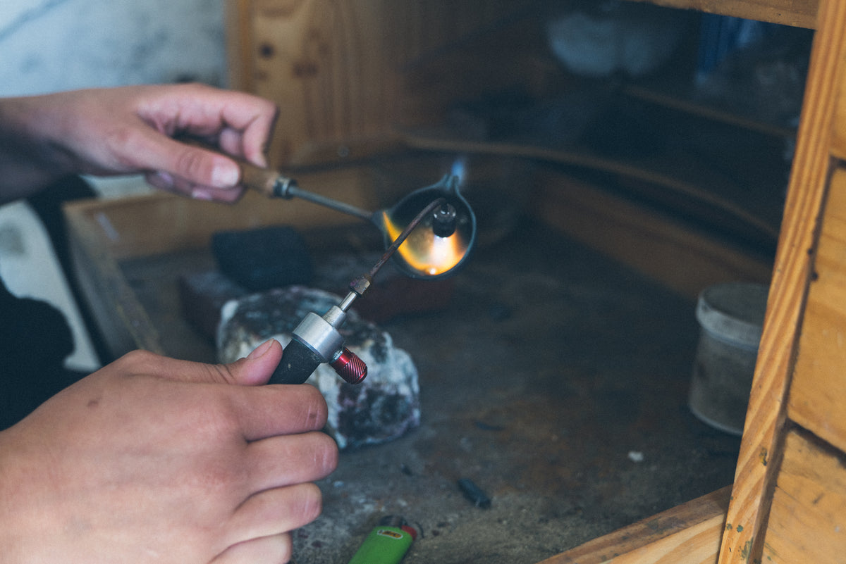 Handcrafting fine jewelry in the studio, with metal being heated and shaped by hand using a jeweler’s torch, showcasing the artisanal process behind Alexis Pavlantos.